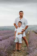 A young man and his son are walking through a beautiful field of lavender and enjoying the fragrance of flowers. Rest and beautiful nature. Lavender blooming and flower picking.