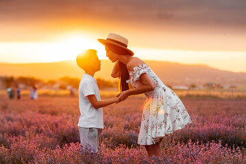 A young beautiful woman with her son is walking through a beautiful field of lavender and enjoying the fragrance of flowers. Rest and beautiful nature. Lavender blooming and flower picking.