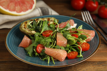 Delicious pomelo salad with grilled avocado served on wooden table, closeup
