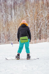 an overweight girl learns to snowboard from  mountainside, view from the back, winter holiday at ski resort
