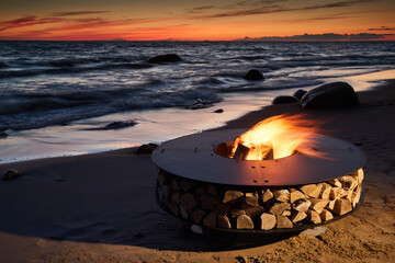 The beautiful metal round a fireplace stands on the sandy coast with a tidal wave at sunset,...