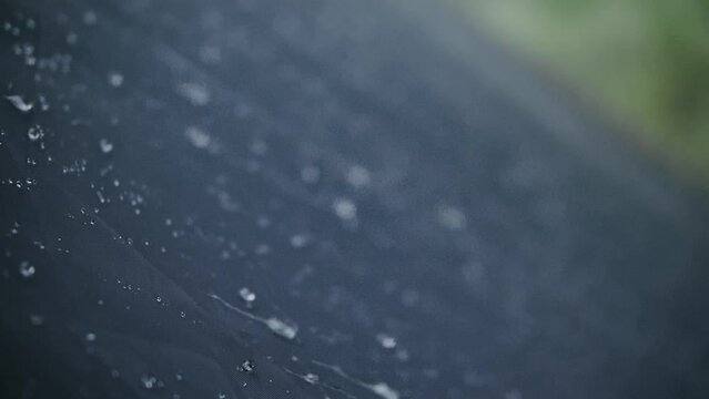 Close-up shot of raindrops water droplets on the tent. Dew drops on texture of fabric of tourist tent in rays of rising or setting sun. Camp, hiking tourism. The rain is pounding on tent. Slow motion
