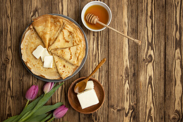 Thin ruddy crepes or pancakes on a plate and on a wooden background. Top view with copy space