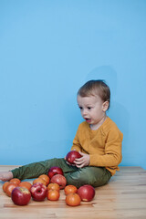 Fototapeta premium a boy of 2 years sits on a wooden table and plays with apples and tangerines, he closes his eyes and plays a game.
