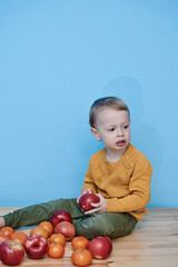 Fototapeta premium a boy of 2 years sits on a wooden table and plays with apples and tangerines, he closes his eyes and plays a game.