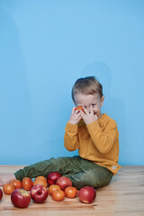 Fototapeta premium a boy of 2 years sits on a wooden table and plays with apples and tangerines, he closes his eyes and plays a game.