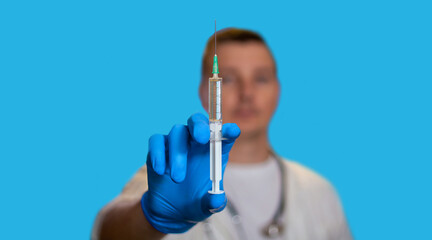 Close-up of the syringe. The doctor holds a syringe in his hands. A young doctor stands on a blue background. A place for text. Medicine.