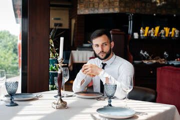 A young bearded male businessman is sitting at a table in a fine restaurant and waiting for his order. Customer service in the catering.