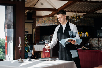 A young male waiter in a stylish uniform is engaged in serving the table in a beautiful gourmet restaurant. A high-level restaurant. Table service in the restaurant.
