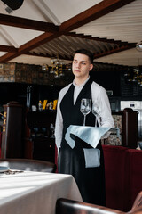 A young male waiter in a stylish uniform is engaged in serving the table in a beautiful gourmet restaurant. A high-level restaurant. Table service in the restaurant.