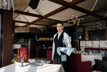 A young male waiter in a stylish uniform is engaged in serving the table in a beautiful gourmet restaurant. A high-level restaurant. Table service in the restaurant.