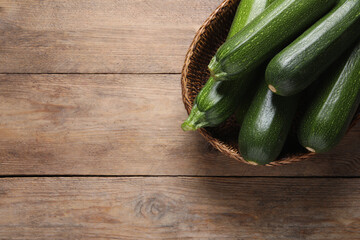 Raw ripe zucchinis in wicker basket on wooden table, top view. Space for text