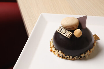 Delicious chocolate dessert decorated with nuts and macaron on table, closeup