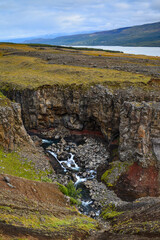 Fototapeta na wymiar A river flowing through a deep ravine near Litlanesfoss and Hengifoss waterfalls, and Lagarfljót lake, East Iceland