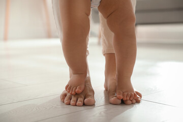 Mother supporting her baby daughter while she learning to walk at home, closeup