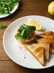 Salmon tartare with avocado, arugula, spinach, bread chips and lemon. On a plate, on a wooden background. Top view. Close up. Healthy healthy food. Raw food. Restaurant.