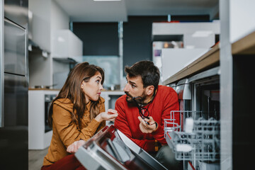 Young couple buying dishwasher in store.