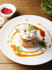 Pork meat in bacon with mushroom sauce, mushrooms. Restaurant serving of a hot meat dish. Hearty food. Lunch for a man. Delicious. Close up. Copy space. Decorated with micro-greens and red pepper peas
