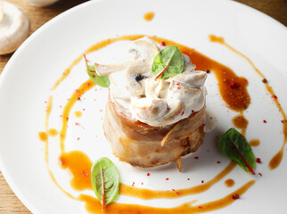 Pork meat in bacon with mushroom sauce, mushrooms. Restaurant serving of a hot meat dish. Hearty food. Lunch for a man. Delicious. Close up. Copy space. Decorated with micro-greens and red pepper peas