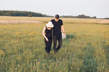 Young pregnant wife and husband walking at field, hold hands together. Couple waiting for baby, relax outdoors