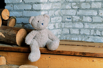A toy gray bear cub sits on wooden steps against a brick wall. Free space on the right for your text