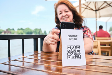 Mature latin woman scanning a QR code with her phone to access a restaurant menu