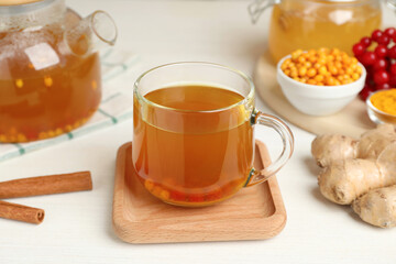 Glass cup of immunity boosting tea with ingredients on white wooden table