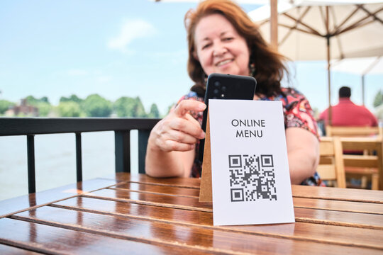 Mature Latin Woman Scanning A QR Code With Her Phone To Access A Restaurant Menu