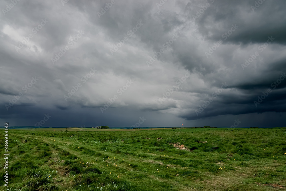 Wall mural a foreboding dramatic dark grey thunder storm cloud sky over an open grass airfield and green meadow