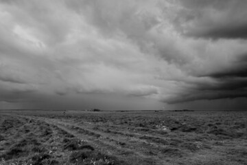 Fototapeta premium a foreboding dramatic dark grey thunder storm cloud sky over an open grass airfield and grass meadows