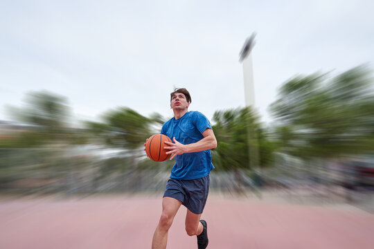 young caucasian man basketball player running to attempting a dunk outdoors