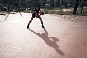 young man playing basketball outdoor on street with long shadows