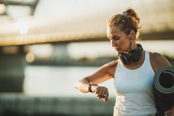 Woman Looking On Smart Watch And Holding Rolled Up Exercise Mat