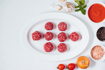 Meatballs in tomato sauce with basil on top. Bright background with ingredients in blurry background. This meal is called Kofte in Turkey and Cufte in Balkans. International meatball day.
