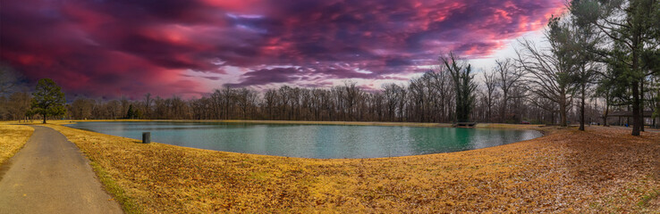 a panoramic shot of a still green lake surrounded by yellow winter grass and bare winter trees with purple sky and powerful clouds at Martin Luther King Riverside Park in Memphis Tennessee USA