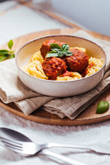 Meatballs in tomato sauce with basil on top. Bright background with ingredients in blurry background. This meal is called Kofte in Turkey and Cufte in Balkans. International meatball day.