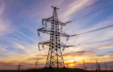 high voltage power lines in the field against the backdrop of a bright and colorful sunset or dawn