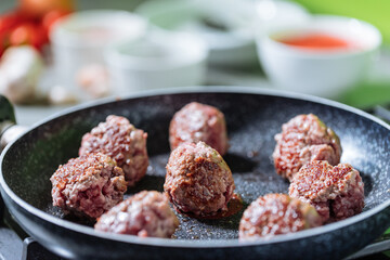 Meatballs in tomato sauce with basil on top. Bright background with ingredients in blurry background. This meal is called Kofte in Turkey and Cufte in Balkans. International meatball day.