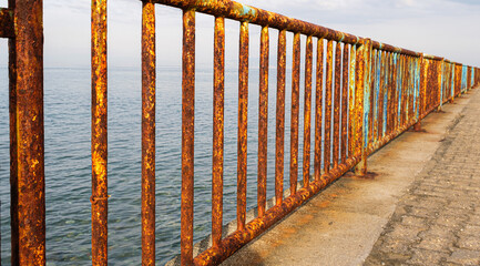 Rusty iron railing, beautiful sea and sky landscape view between oxidized railings gap.