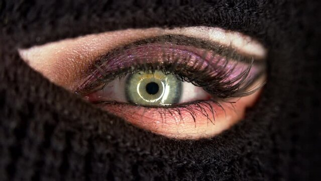 Macro view of female eye, she in black balaclava dressed as hacker. Reflection of explosion on face. Concept of mass rallies, riots, robbery. Mandatory conscription, military theme.