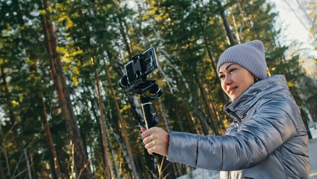 Woman Holding On Handheld Film 3-axis Gimbal Stabilization Device in Winter for Smartphone. Girl Blogger Make Selfie, Broadcast Video Blogging, Vlogging. Videographer Operator Take Photo Video.