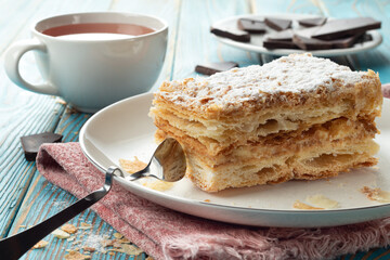 Napaleon cake on a white dish with black tea and chocolate wooden background