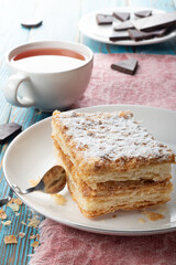 Napaleon cake on a white dish with black tea and chocolate wooden background