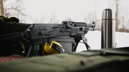 Thermos next to shooting headphones and a civilian Kalashnikov assault rifle in Winter