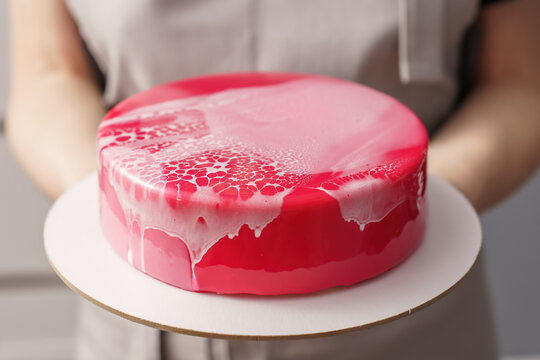 A female pastry chef holds beautiful red mousse cake on her outstretched arms. Selective focus.
