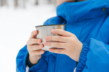 Child hands holds a cup. Child drinking a cup of tea on the street while walking. Winter walk