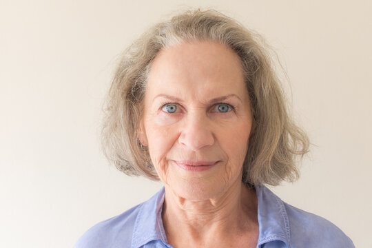 Close up portrait of senior woman with grey hair and blue eyes against neutral background (selective focus)