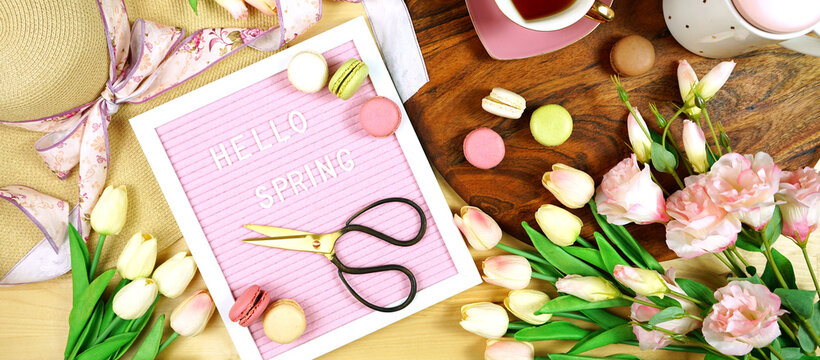Hello Spring theme creative layout concept flat lay tea break with pink tulips and lisianthus flowers, sun hat on wooden table background. Sized to fit popular social media and web banner.