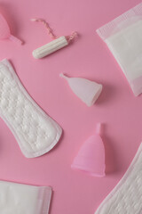 Different types of feminine menstrual hygiene materials products such as pads cloths tampons and cups. Pink background vertical