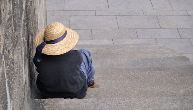 Mendigo sentado numas escadas à espera de uma esmola - sem abrigo com um chapéu - escadas em pedras - degraus